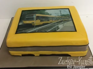 Rechteckige gelbe Torte mit Foto-Druck einer Stuttgarter Stadtbahn (U-Bahn) auf Schienen.