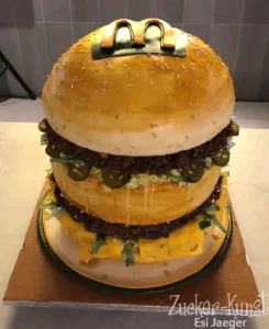 realistische Torte in Form eines McDonald's Big Mac Burgers, verziert mit einem essbaren M-Logo, Salat, Käse und Gewürzgurken.