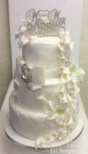Dreistöckige Hochzeitstorte in reinem Weiß mit Zuckerblumen, Schleife und Strass-Brosche. Klassische Eleganz.