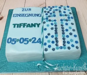 Torte in Form eines blauen Buches zur Taufe von Tiffany, mit Kreuz aus Blumen und Datum 05.05.24.