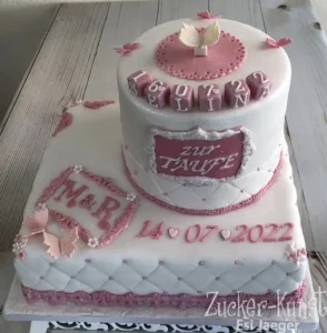 Zweistöckige weiße Tauftorte mit Pink-Akzenten, Tauben-Figur und dem Namen, mit Kreuz-Stepp-Muster.