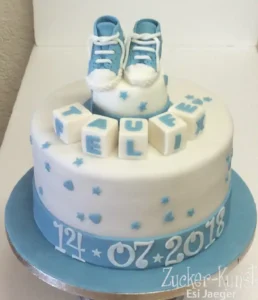 Runde Tauftorte Jungen in Blau und Weiß, dekoriert mit Babyschuhen, Würfeln und dem Datum der Taufe.