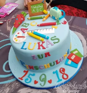 Runde blaue Einschulungstorte, reich verziert mit Schultüte, ABC-Buchstaben, Buntstiften und Schulranzen-Deko.