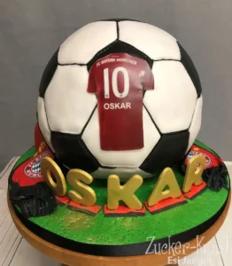 Coole Geburtstagstorte für Jungs in Form eines Fußballs, mit FC Bayern Logo und goldenem Namensschriftzug.