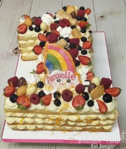Zahl 1 Torte für Mädchen, belegt mit frischen Beeren, Baiser und einem Regenbogen-Topper, personalisiert mit Amelie.