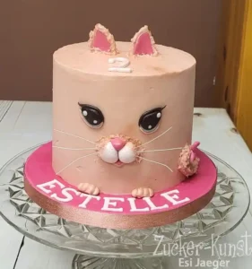 Torte in Form eines Katzenkopfs mit rosa Ohren und der Zahl 2, personalisiert für Estelle auf einem pinken Tortenteller.