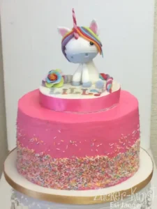 Zweistöckige pinke Einhorn Torte mit Regenbogenmähne und personalisiertem Namensband für Lilly.