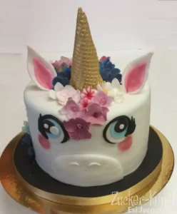 Runde Einhorn Torte mit goldenem Horn, pinken Ohren und Blüten-Dekoration für einen Mädchen-Geburtstag.