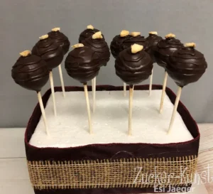 Dunkle, handgetauchte Cake Pops mit Schokostreifen und Nuss-Topping in rustikaler Bändchenbox
