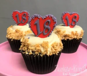 Drei 18. Geburtstags-Cupcakes mit rotem Herz-Topper und gerösteten Kokosflocken