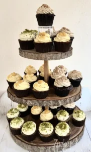 Dunkle Schoko Cupcakes mit hellem Frosting und verschiedenen Toppings wie Karamell und grünen Pistazien-Streuseln.