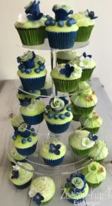 Cupcakes mit grünem und blauem Frosting, dekoriert mit filigranen Zuckerblumen und Beeren