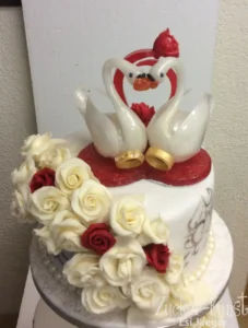 Zuckerfiguren: Schwäne mit Goldringen als Torten-Topper, umgeben von weißen und roten Zuckerrosen auf einer Hochzeitstorte.