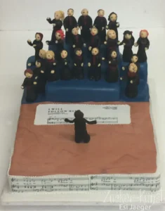 Zuckerfiguren: Chor mit Dirigent, Sängerfiguren auf gestuftem Podest und Notenblättern (I Will Follow Him).